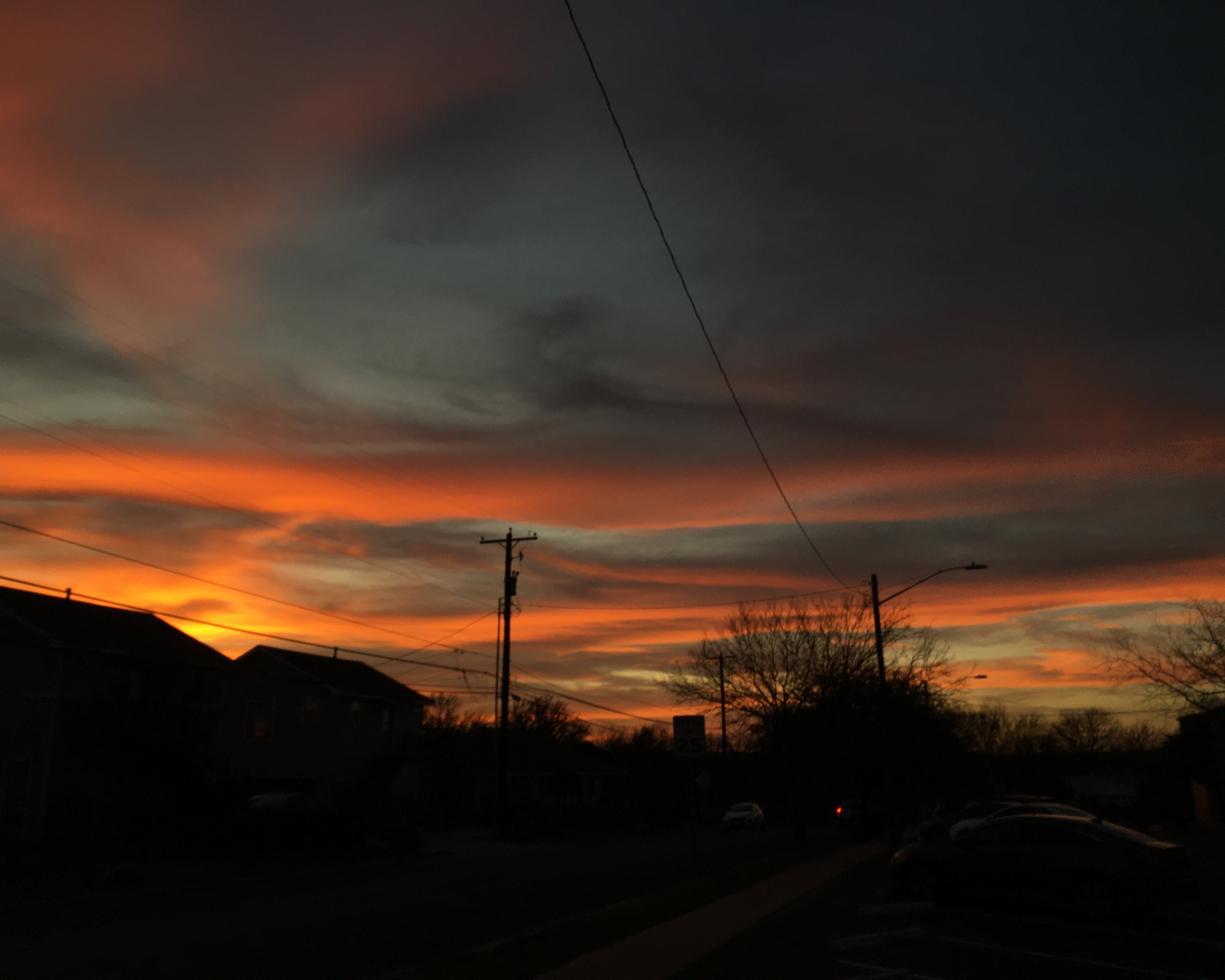 photo of a vivid, bursting orange sunset, with the silhoutte of some houses visible in the fregroun
